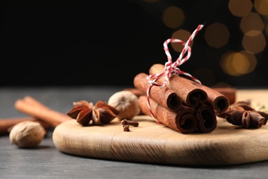 Cinnamon sticks and other spices on table against black background with blurred lights, closeup