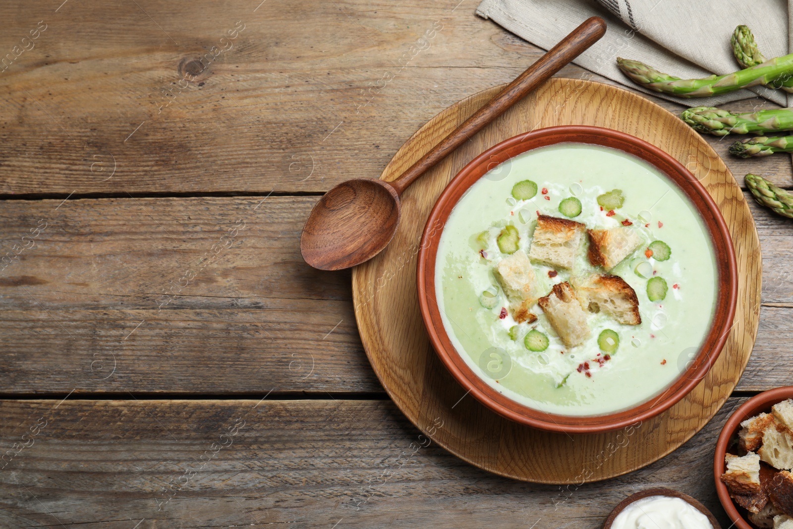 Photo of Delicious asparagus soup with croutons served on wooden table, flat lay. Space for text