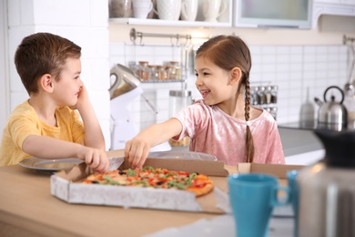 Cute little kids eating tasty pizza at home