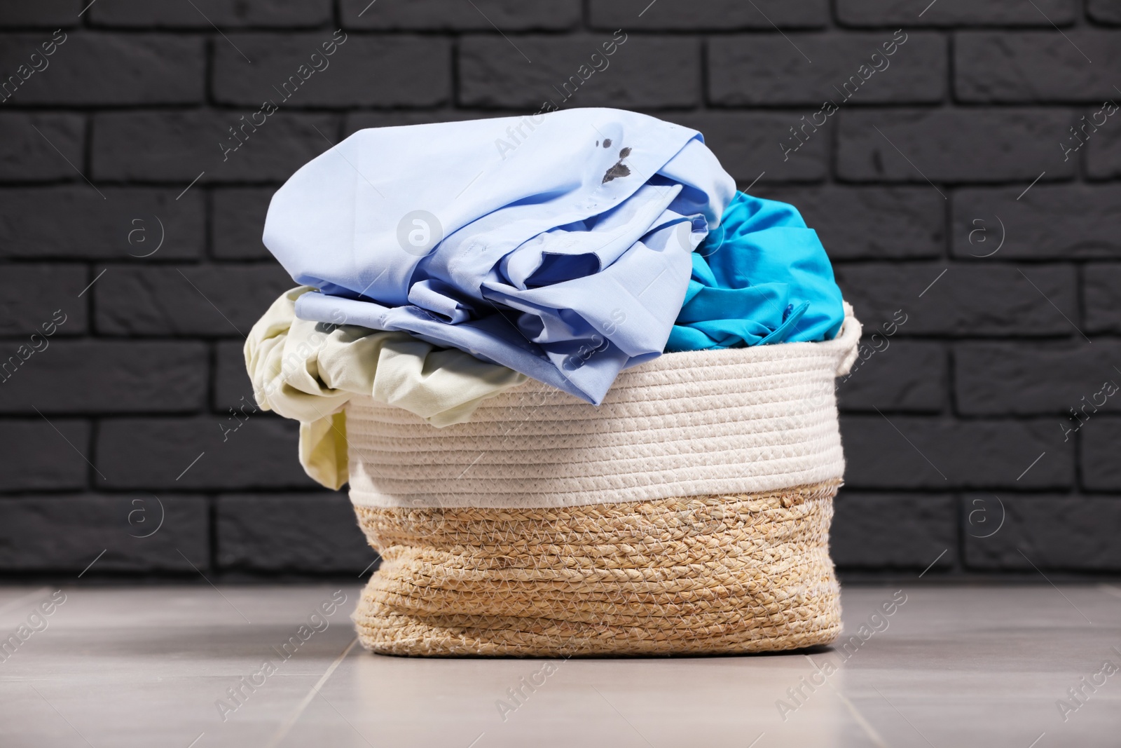 Photo of Laundry basket with clothes near black brick wall