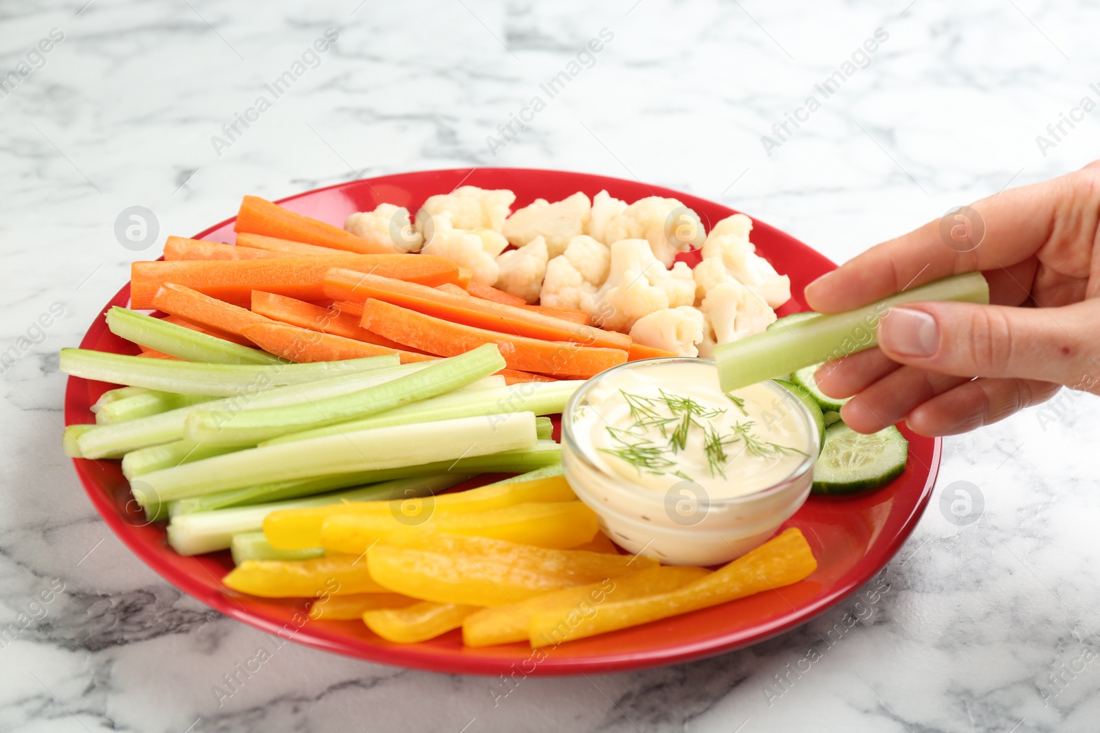 Photo of Woman dipping celery stick in sauce at white marble table, closeup