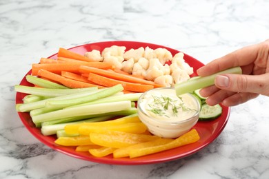 Woman dipping celery stick in sauce at white marble table, closeup