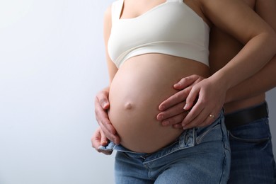 Photo of Man touching his pregnant wife's belly on light background, closeup. Space for text