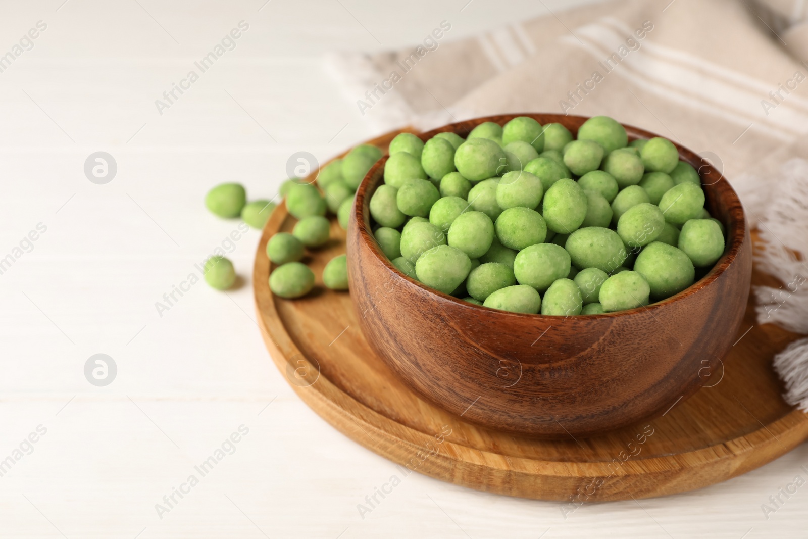 Photo of Tasty wasabi coated peanuts on white wooden table, space for text