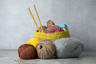 Soft woolen yarns and knitting needles on grey table