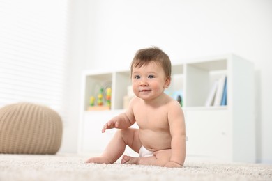 Cute baby boy sitting on carpet at home, low angle view