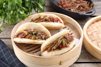 Photo of Delicious gua bao in bamboo steamer on wooden table, closeup