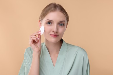 Photo of Young woman cleaning her face with cotton pad on beige background