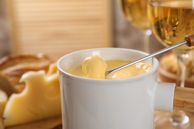 Pot of tasty cheese fondue and fork with bread on table