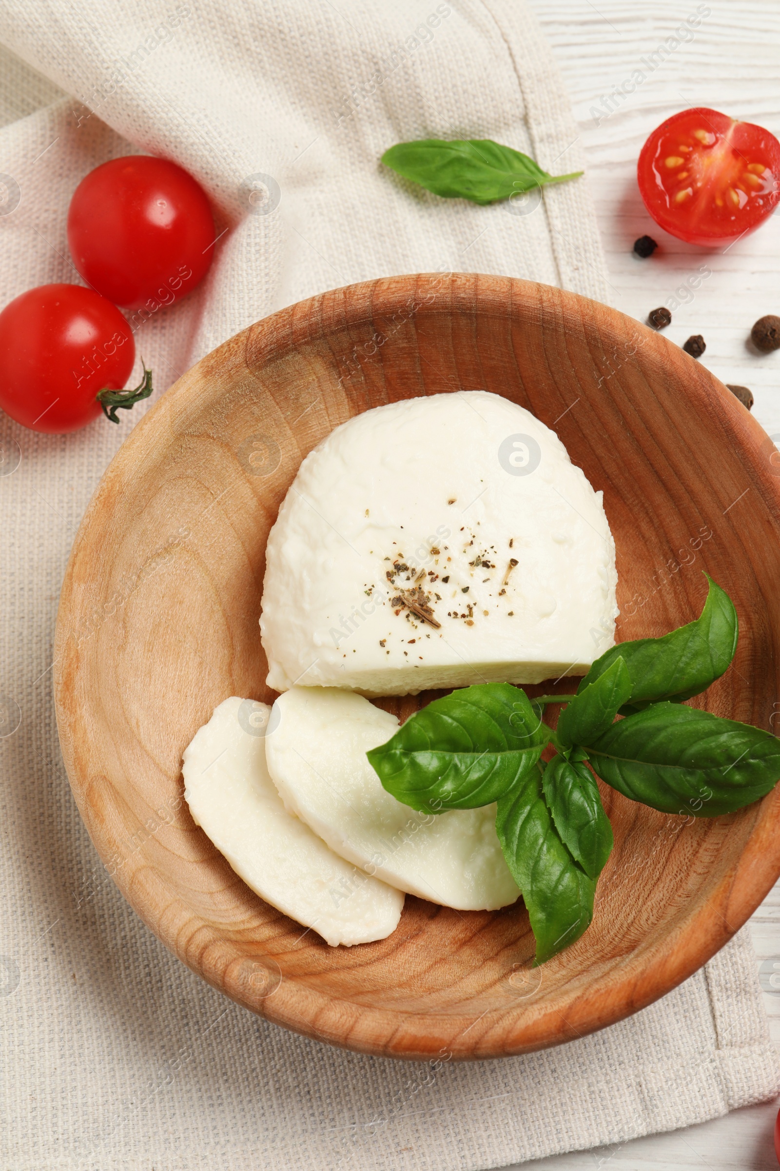 Photo of Delicious mozzarella with tomatoes and basil leaves in wooden bowl on table, flat lay
