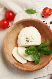 Delicious mozzarella with tomatoes and basil leaves in wooden bowl on table, flat lay