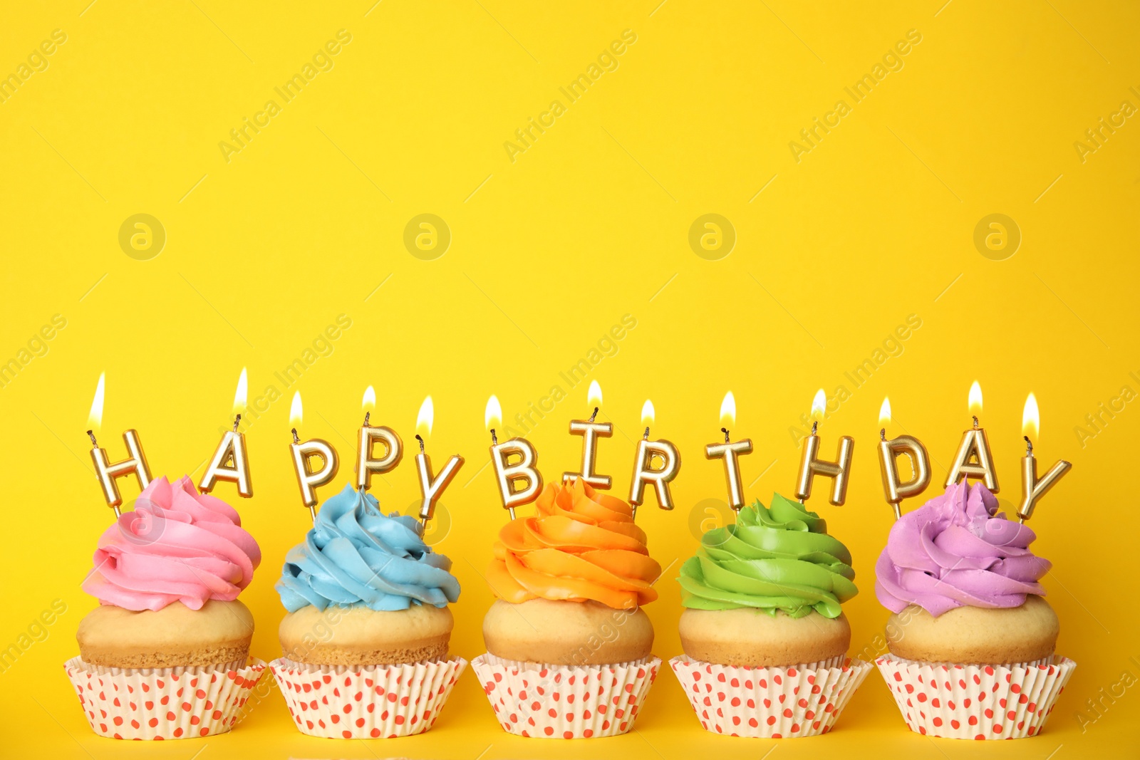 Photo of Birthday cupcakes with burning candles on yellow background. Space for text