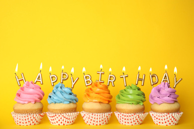 Birthday cupcakes with burning candles on yellow background. Space for text