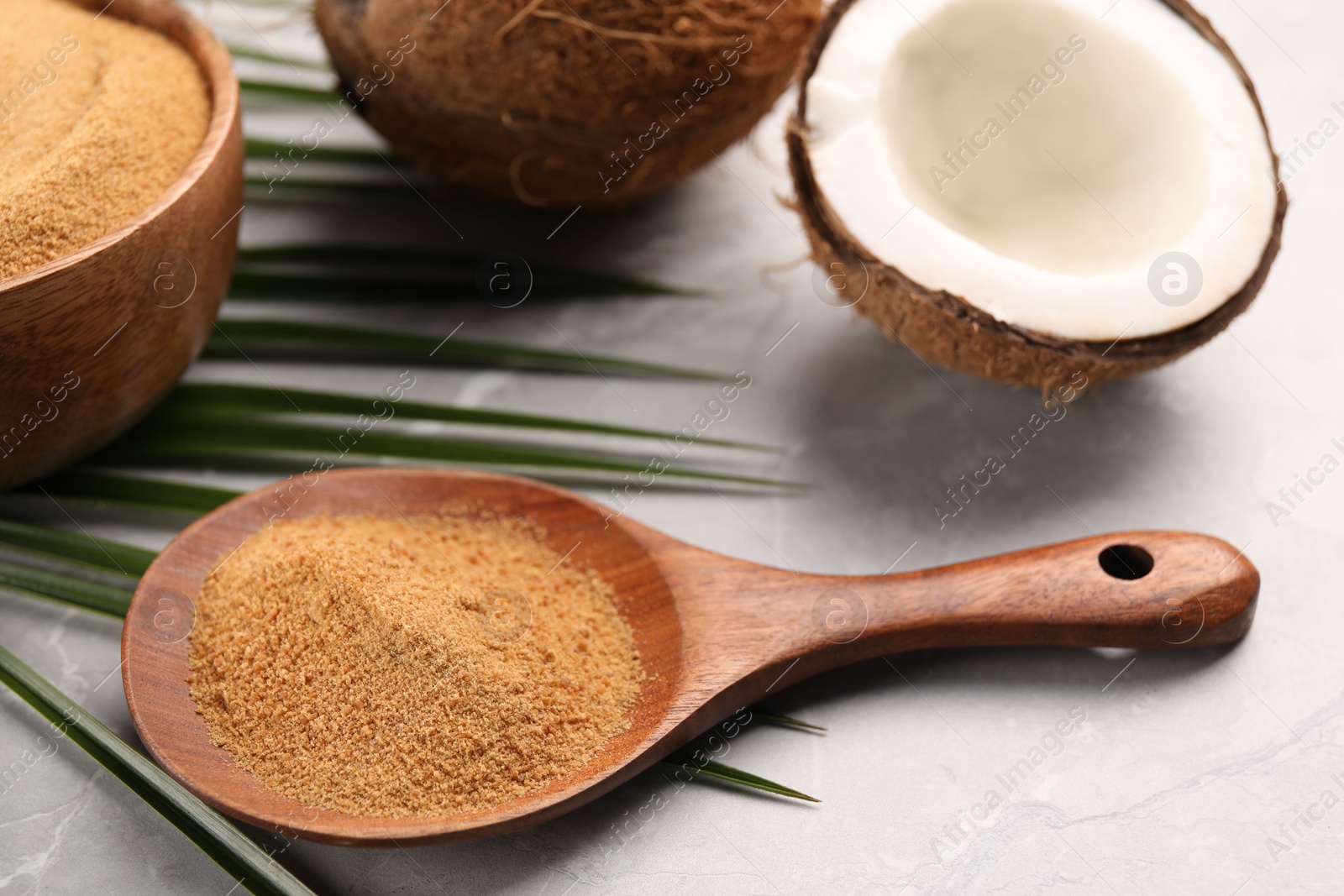 Photo of Spoon with coconut sugar, palm leaves and fruit on light marble table, closeup