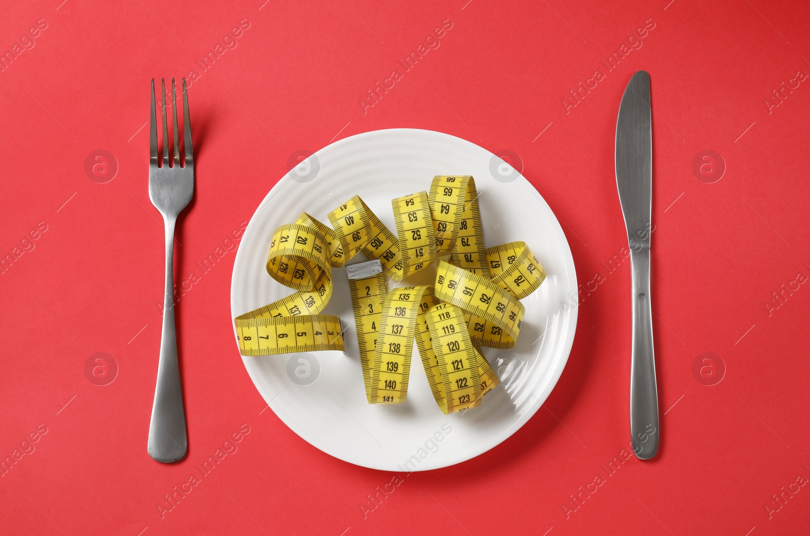 Photo of Plate, cutlery and measuring tape on red background, flat lay. Diet concept