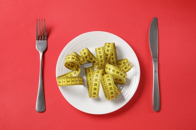 Photo of Plate, cutlery and measuring tape on red background, flat lay. Diet concept