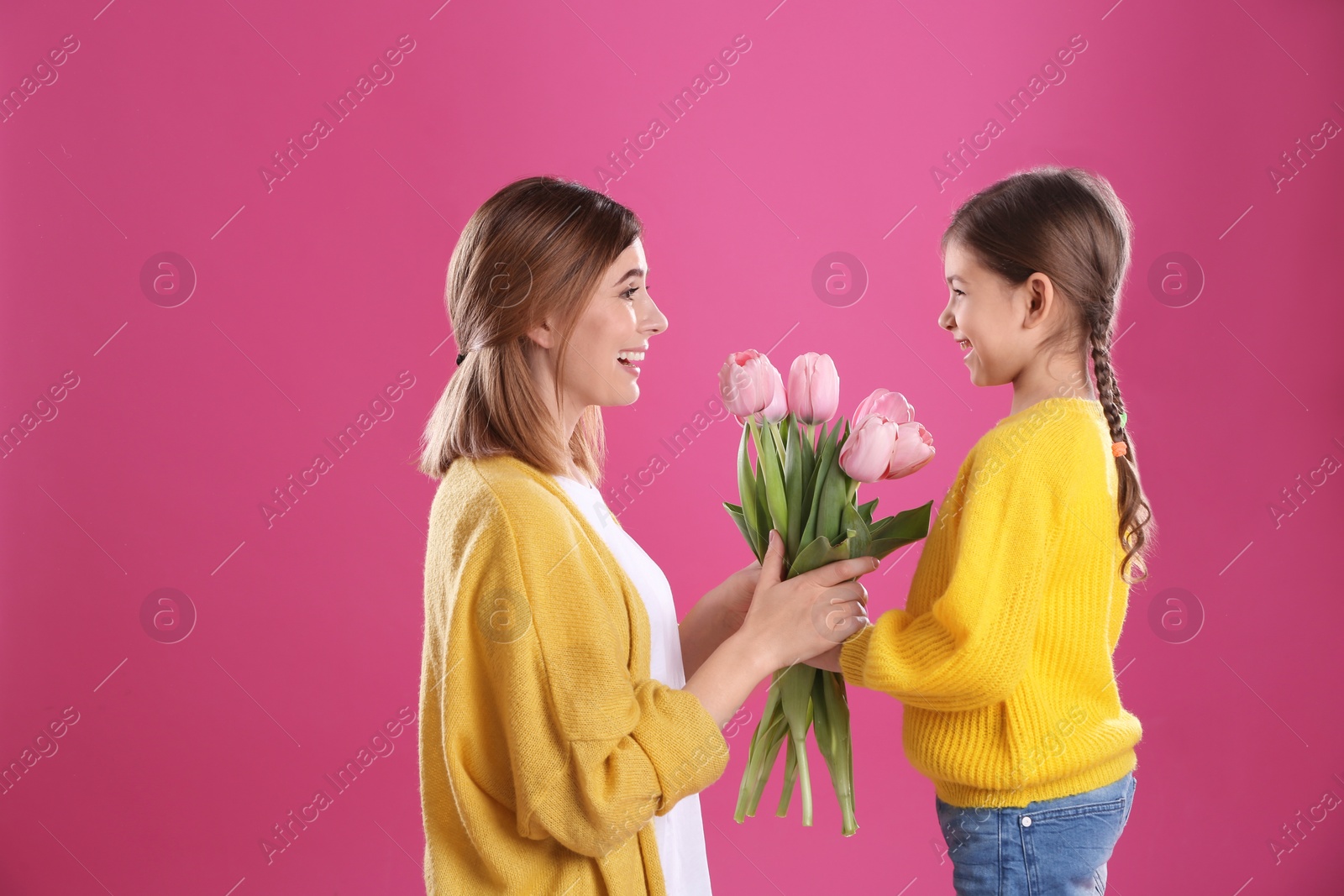Photo of Happy mother and daughter with flowers on color background. International Women's Day