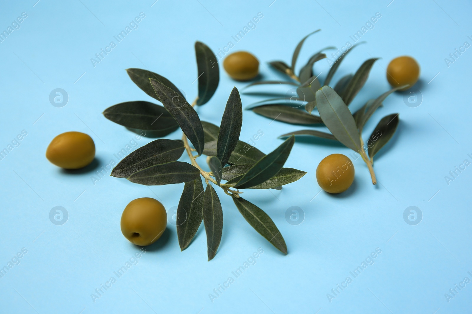 Photo of Fresh olives and green leaves on light blue background, closeup