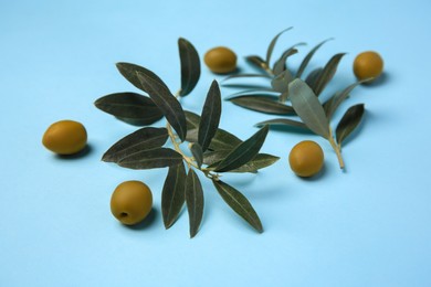 Photo of Fresh olives and green leaves on light blue background, closeup