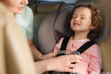 Mother fastening her sleeping daughter in child safety seat inside car