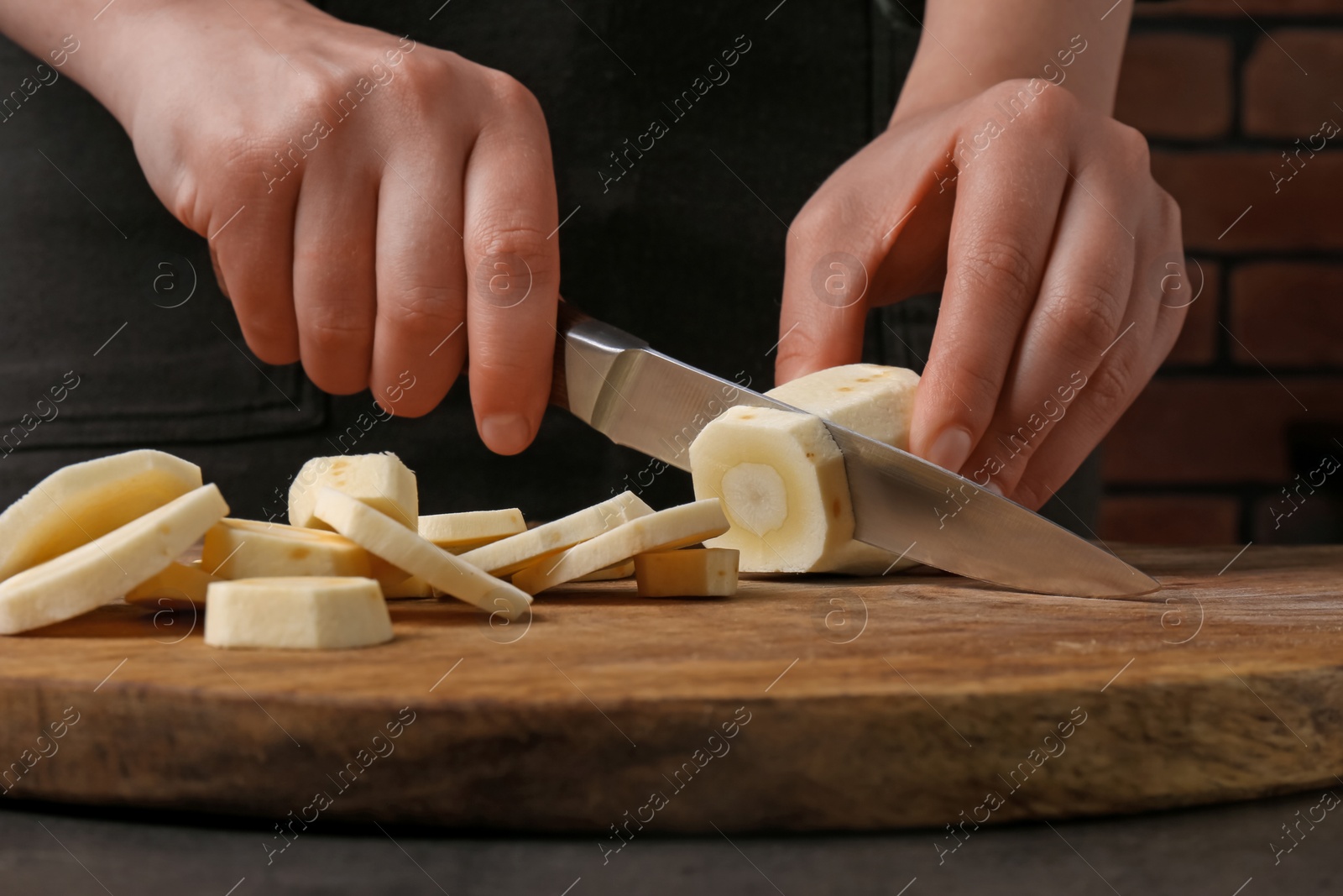 Photo of Woman cutting delicious fresh ripe parsnip at black table, closeup