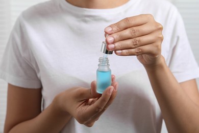 Photo of Woman with bottle of cosmetic serum and dropper on light background, closeup