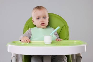 Photo of Cute little baby with yogurt in high chair on gray background