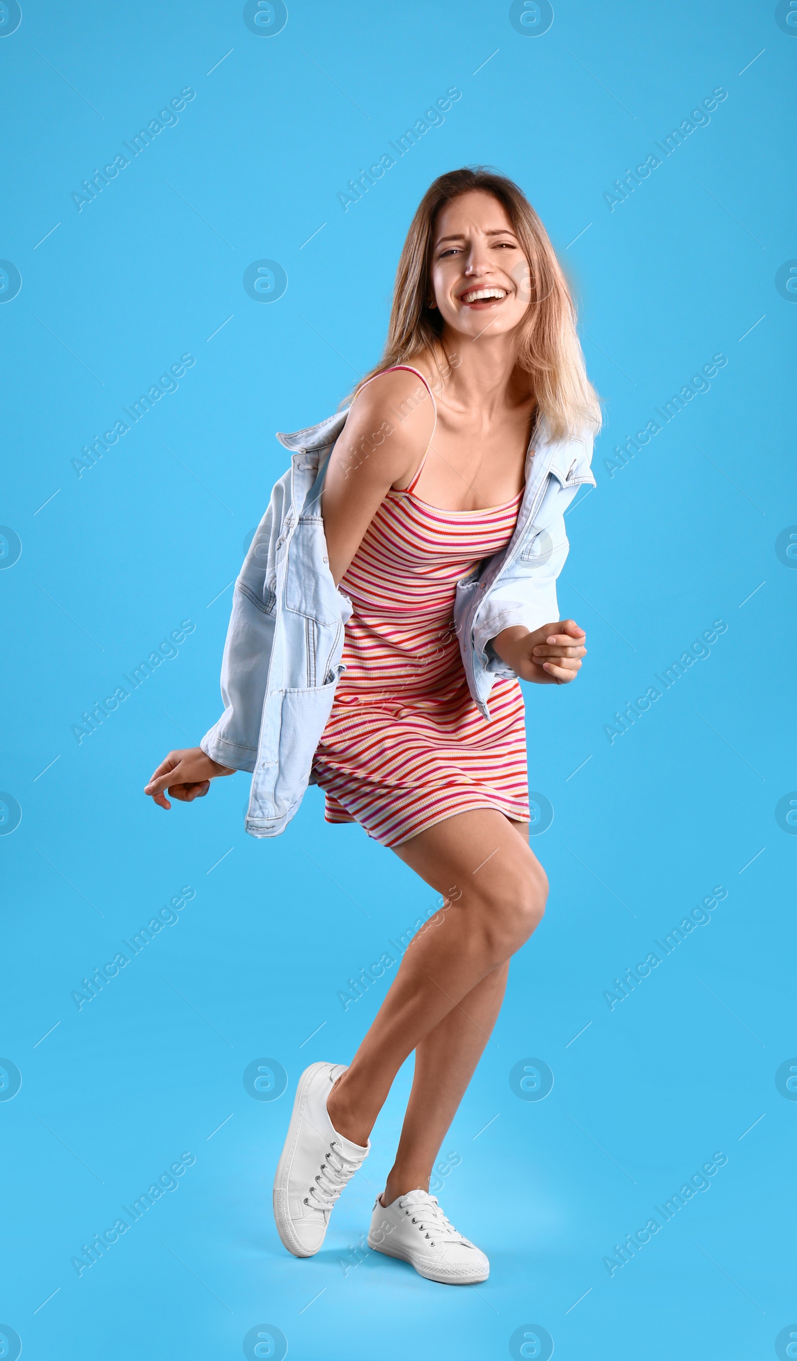 Photo of Beautiful young woman in dress and jacket dancing on blue background