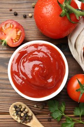 Photo of Delicious ketchup in bowl, tomatoes and peppercorns on wooden table, flat lay