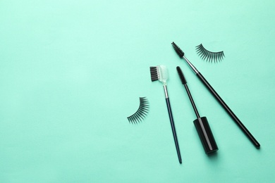 Photo of False eyelashes and brushes on turquoise background, flat lay. Space for text