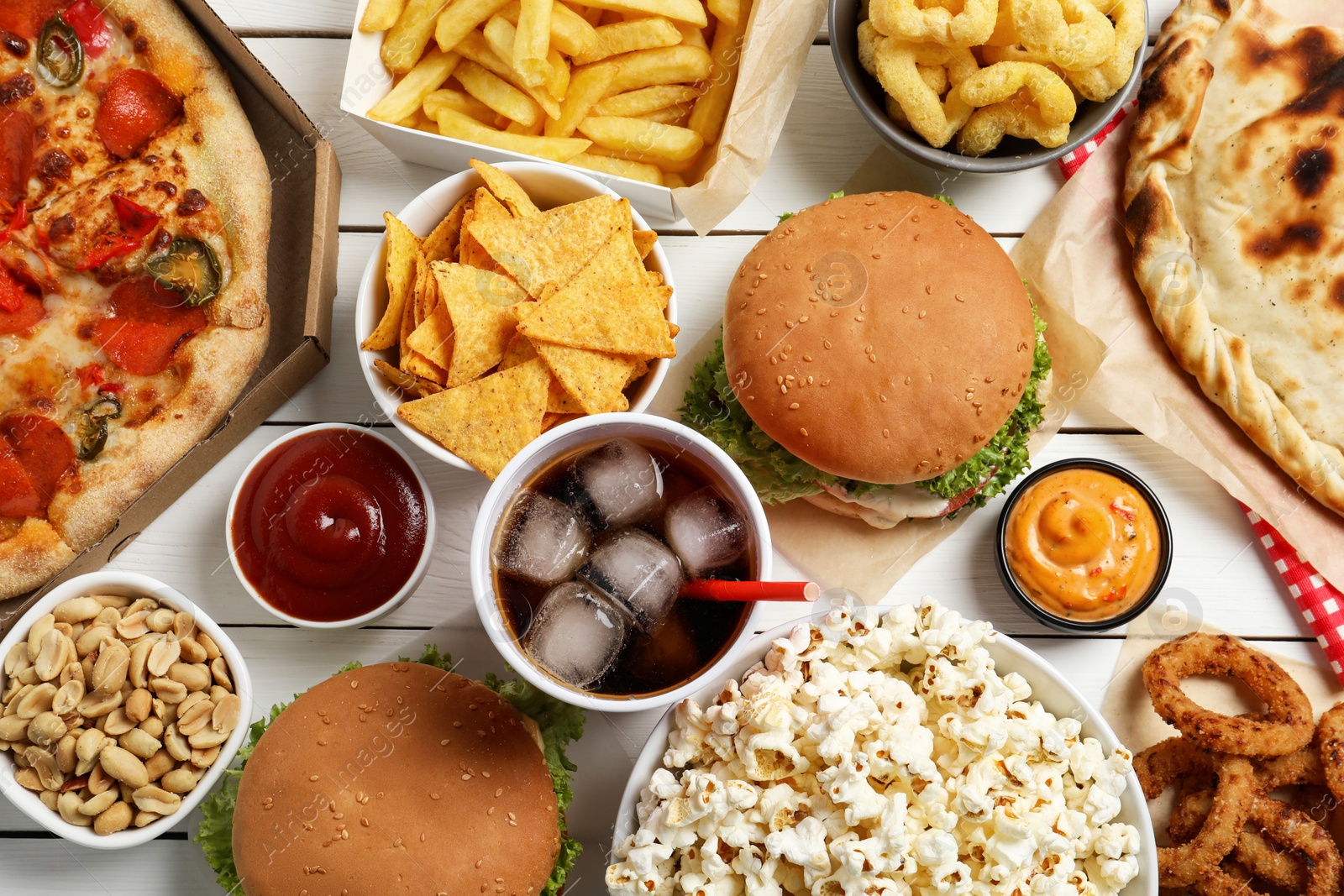 Photo of Burgers, chips and other fast food on white wooden table, flat lay