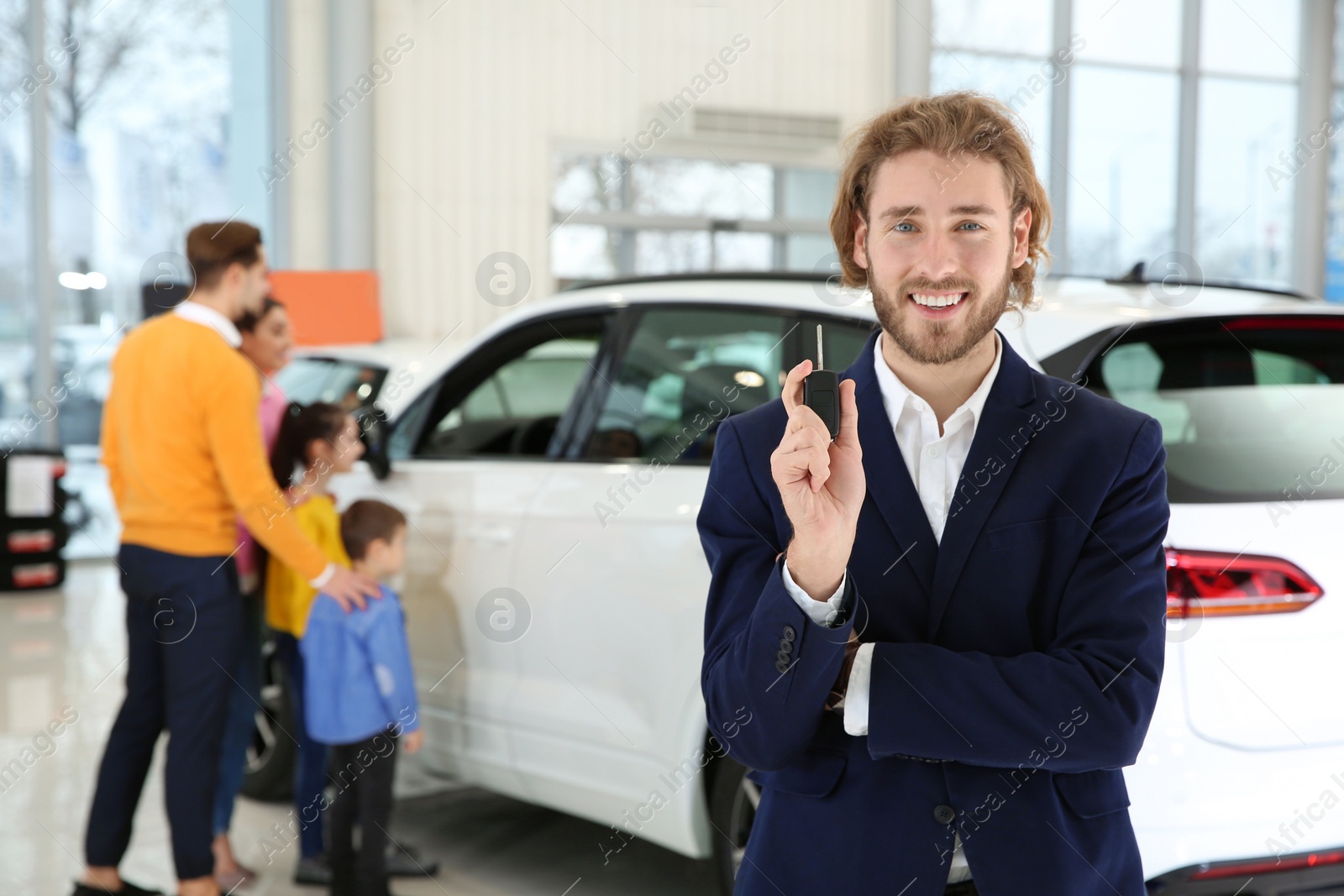Photo of Car salesman with key and blurred family near auto on background