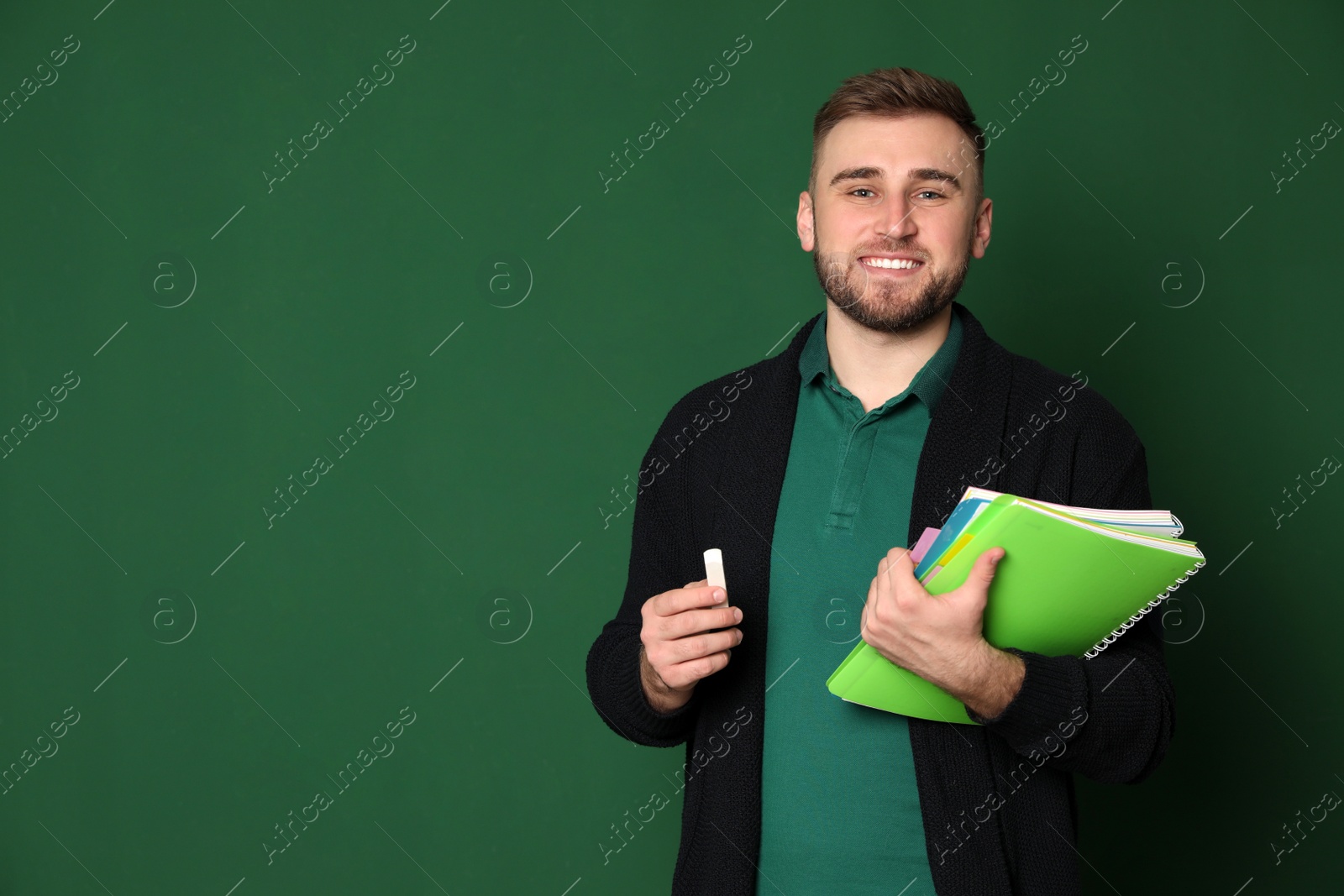 Photo of Portrait of young teacher with notebooks and chalk on green background. Space for text