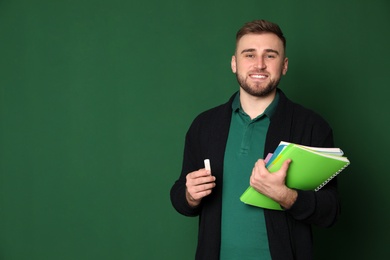 Portrait of young teacher with notebooks and chalk on green background. Space for text