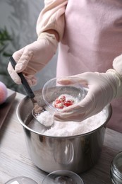 Photo of Woman in gloves making bath bomb at wooden table indoors, closeup