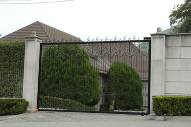 Beautiful stone fence with ornate black metal gates around house and garden