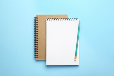 Photo of Notebooks and pencil on light blue background, top view