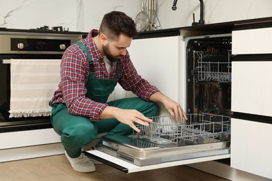 Photo of Serviceman examining dishwasher lower rack in kitchen