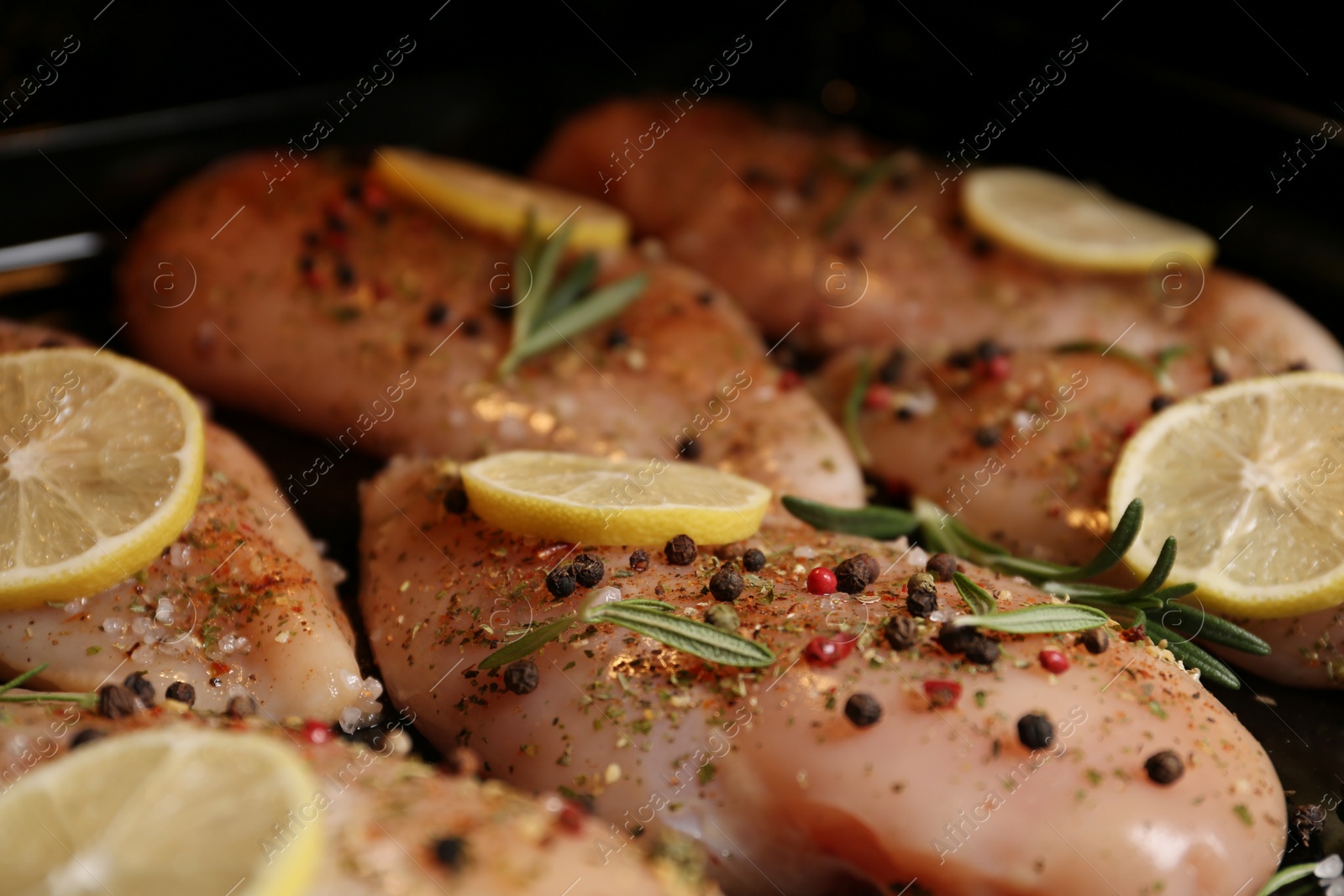 Photo of Chicken breasts with lemon and rosemary on baking sheet, closeup