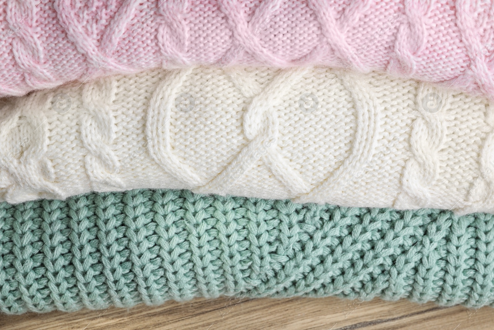 Image of Stack of folded warm sweaters on wooden table, closeup