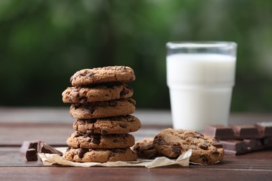 Photo of Delicious chocolate chip cookies and glass of milk on wooden table