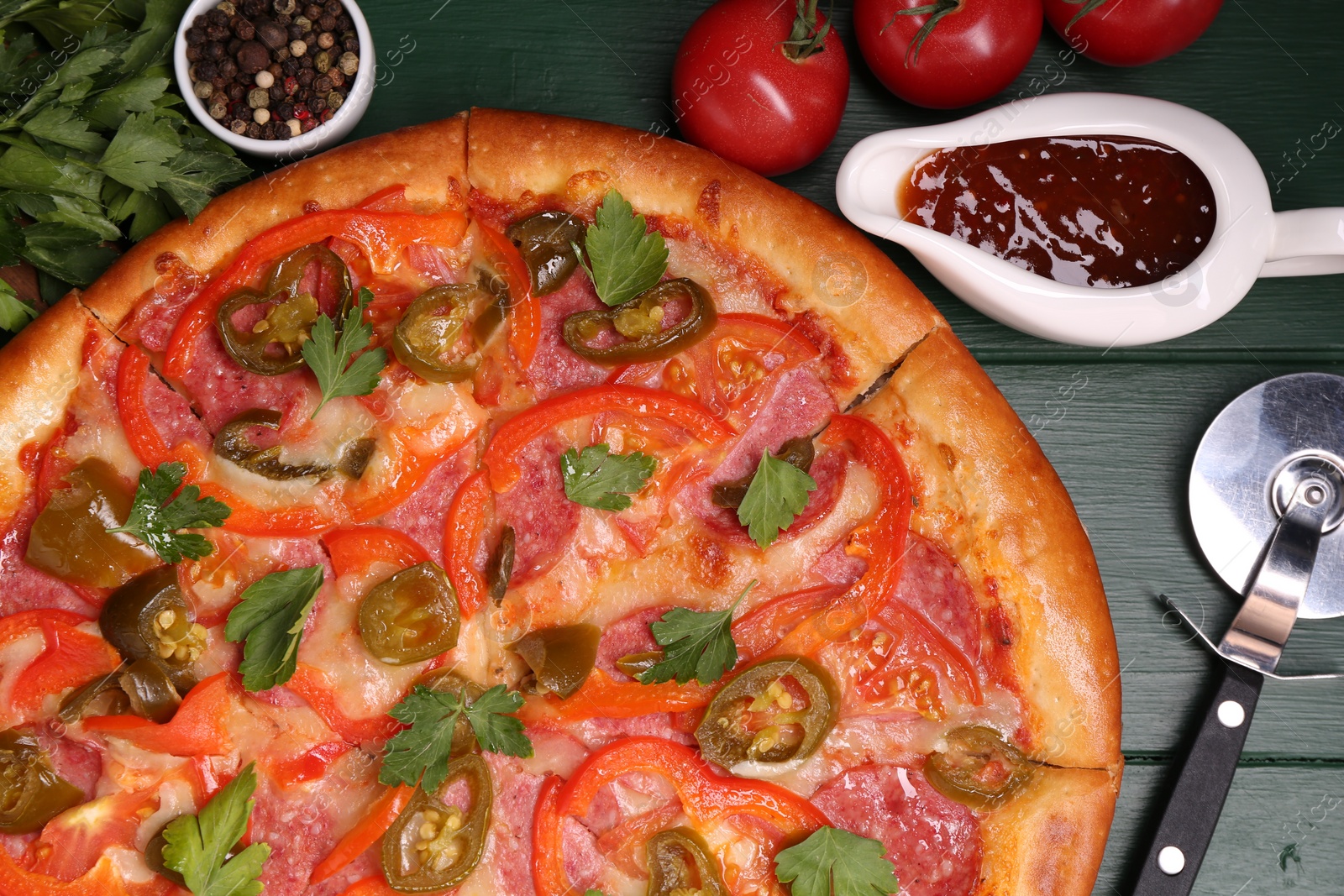 Photo of Delicious pizza Diablo, ingredients and cutter on green wooden table, flat lay