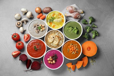 Photo of Tasty broth, different cream soups in bowls and ingredients on gray table, flat lay