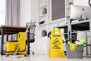 Photo of Cleaning service. Mop, wet floor sign and bucket with supplies in office