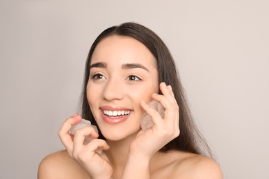 Photo of Young woman with ice cubes on light background. Skin care