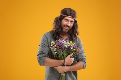 Photo of Hippie man with bouquet of colorful flowers orange background
