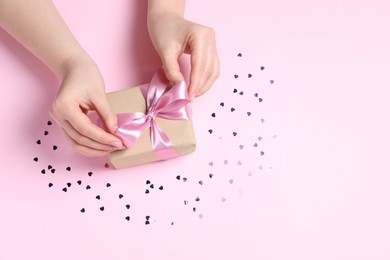 Woman with gift box and confetti on pink background, above view. Space for text