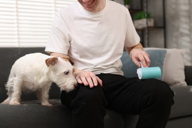 Photo of Pet shedding. Smiling man with lint roller removing dog's hair from pants at home, closeup