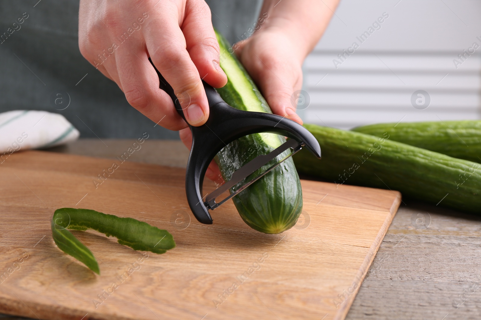 Photo of Woman peeling cucumber at wooden table indoors, closeup