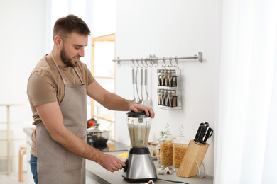 Young man using blender to cook cream soup in kitchen